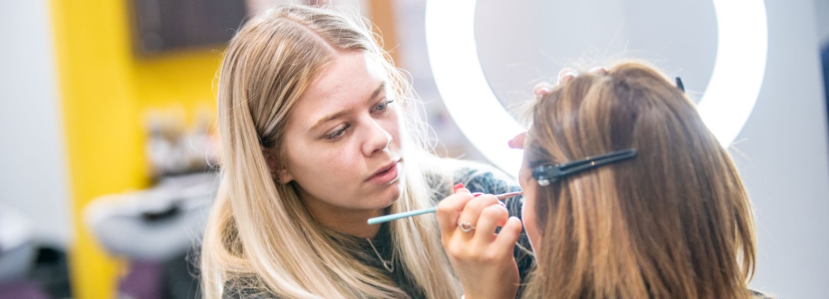 student applying makeup to another student