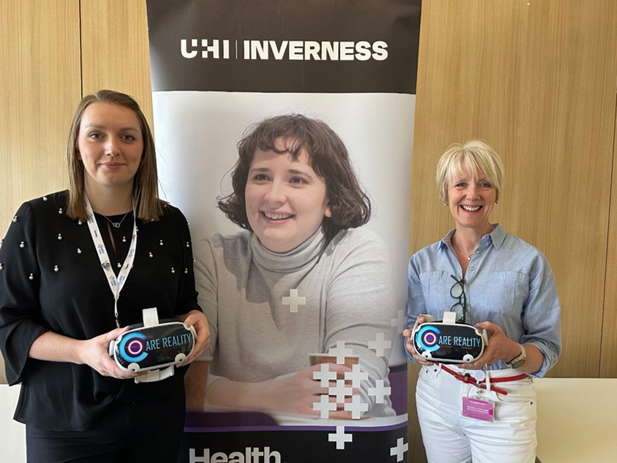 Two women standing by a UHI Inverness banner wearing headsets Two women standing by a UHI Inverness banner wearing headsets